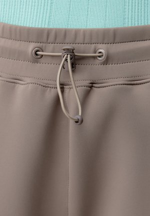 Harmaa joustava vyötärönauha, jossa on säädettävä nyöri ja lukko beigen värisellä kankaalla, korostaen yksityiskohtaista ompelua ja tekstuuria.