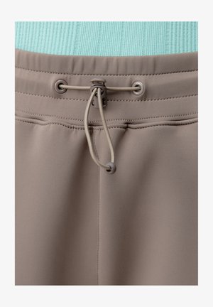 Grijze elastische tailleband met verstelbare trekkoord en schuifknop op beige stof, met gedetailleerde stiksels en textuur.