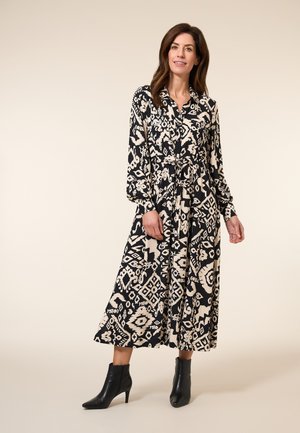 Zwart en crèmekleurig gestreept jurk met lange mouwen, een knopenfront en een tailleceintuur. Gecombineerd met zwarte enkellaarsjes. Gladde stoftextuur.