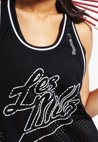 Schwarzes Netz-Trägershirt mit weißem "Les Mills" Grafikdruck, umrandet von einem weißen Saum am Halsausschnitt und den Armlöchern. Reebok-Logo an der Seite.