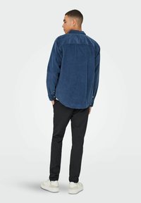 Marinblå corduroy skjorte med button-down krave, lange ærmer og rund kant, parret med sorte bukser og hvide sneakers.