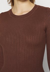 Brun ribbad stickad topp med rund halsringning. Tyget har vertikala ränder och ett subtilt skimrande utseende som ger en texturerad effekt.