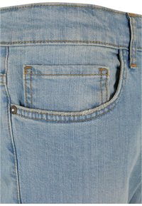 Vaaleansinisiä farkkuja, joissa on takatasku, metallinäkötihkalla ja näkyvillä saumoilla. Kankaan pinta on haalistunut ja kuluneen näköinen.