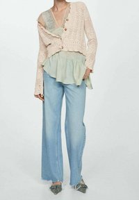 Světle růžový pletený svetr s knoflíky, vrstvený mátově zelený peplum top, modré široké džíny s zubatými lemy a vzorované ploché boty.