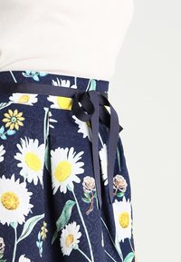 Floral skirt featuring a navy background with large white daisies, yellow accents, and a navy ribbon belt tied at the waist.