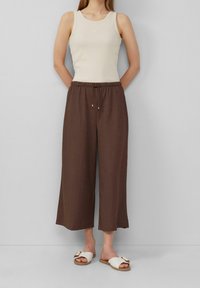 Beige pruhované tílko spárované s hnědými volnými culottes, které mají elastický pas a boční kapsy, doplněné bílými sandalemi na slip.