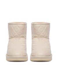 Botas de tobillo acolchadas en color beige con un exterior de cuero suave, puntera redonda y suela texturizada. Presentan costuras decorativas y una altura baja.