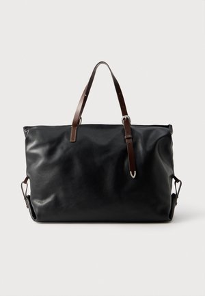 Grand sac cabas en cuir noir avec des anses d’épaule brunes et des fermoirs latéraux argentés, présenté sur un fond clair uni.