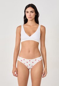 Bralette blanca con un diseño de escote en V y tirantes anchos, combinado con braguitas blancas acanaladas que presentan un estampado de fresas.