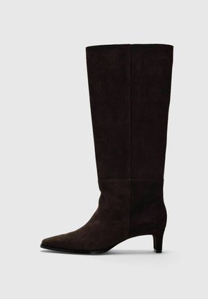 Botte en daim marron foncé montant jusqu’au genou, à bout pointu, talon bas et tige droite, présentée de profil.