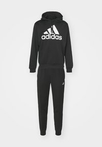 Czarna bluza z kapturem i dopasowane spodnie wykonane z miękkiego materiału, z dużym białym logo adidas z przodu oraz małym logo na nogawce spodni.