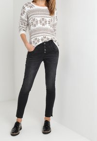 Bílé svetr s vzorem sněhové vločky v béžové barvě, doplněný o černé slim kalhoty s knoflíkovým zapínáním a černé boty s platformou.