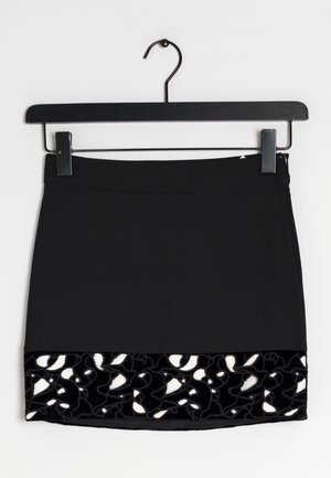 Falda negra con una textura suave y un borde de encaje en negro y blanco de terciopelo en el dobladillo. Cuelga de un perchero de metal negro.