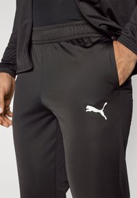 Μαύρο αθλητικό παντελόνι από απαλό, ελαφρύ ύφασμα, με ελαστική μέση και λευκό λογότυπο Puma στο μηρό.