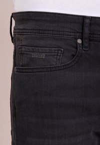 Svarta denimjeans med en mellanläggdesign, subtil textur, tonade sömmar och en metallisk 'BOSS'-logotyp på framfickan.