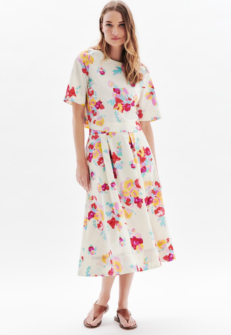 Robe midi florale à manches courtes, avec un fond crème clair et des fleurs vibrantes roses, jaunes et bleues, et une jupe plissée.