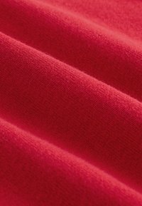 Gros plan sur un tissu rouge doux avec une texture tissée visible et des plis délicats.