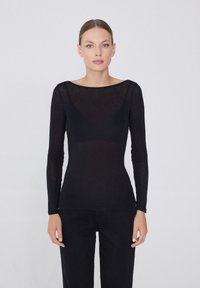 Haut noir à manches longues en tissu transparent avec un col bateau, coupe slim, et texture lisse, associé à un pantalon noir.