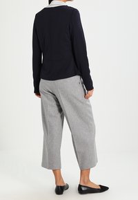 Tukevasti istuva laivastonsininen bleiseri, jossa on sileä pinta, yhdistetty pehmeästä kankaasta tehtyihin harmaisiin leveälahkeisiin housuihin ja mustiin mataliin kenkiin.