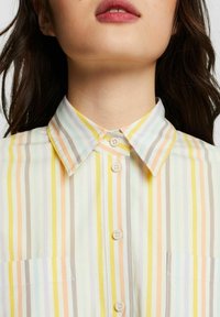 Ljus, kragarskjorta med vertikala ränder i pastellfärger (gult, orange, ljusblått, grått) med knäppning fram och ficka.