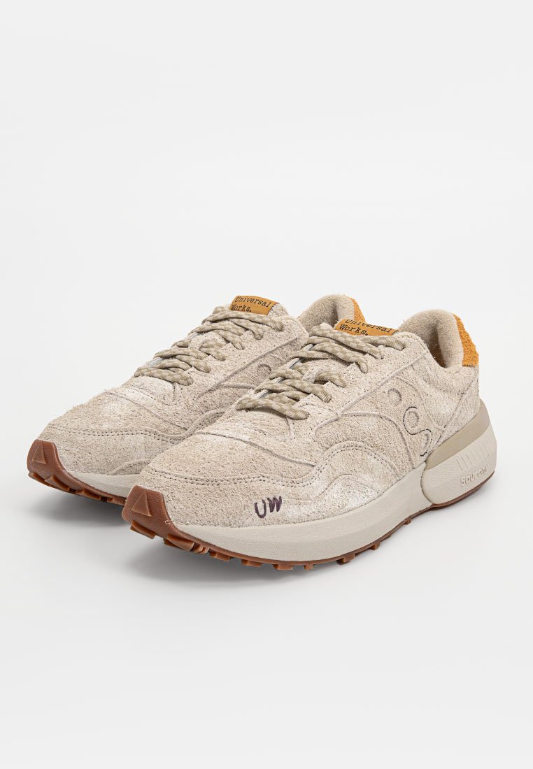 Sneakers beige in suede con finitura testurizzata e suola in gomma marrone. Presentano lacci tondi, colletto imbottito e logo sulla linguetta e sul lato.