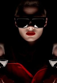 Schwarze, übergroße Sonnenbrille mit kantigem Design, kombiniert mit kräftigen roten Lippen und einem roten Mantel vor einem dunklen Hintergrund. Die Textur hebt eine matte Oberfläche hervor.