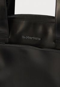 Μαύρη τσάντα χειρός από λείο, ανθεκτικό υλικό με κλείσιμο με φερμουάρ, ραμμένες λεπτομέρειες και ανάγλυφο λογότυπο στο μπροστινό μέρος.