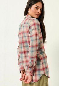 Flannel shirt featuring a blue, red, and cream plaid pattern, long sleeves, a shirttail hem, and button details on the cuffs.