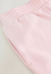 Pantalones de chándal de algodón rosa que presentan una cinturilla elástica acanalada y una textura suave. Incluyen bolsillos laterales y un diseño de corte relajado.