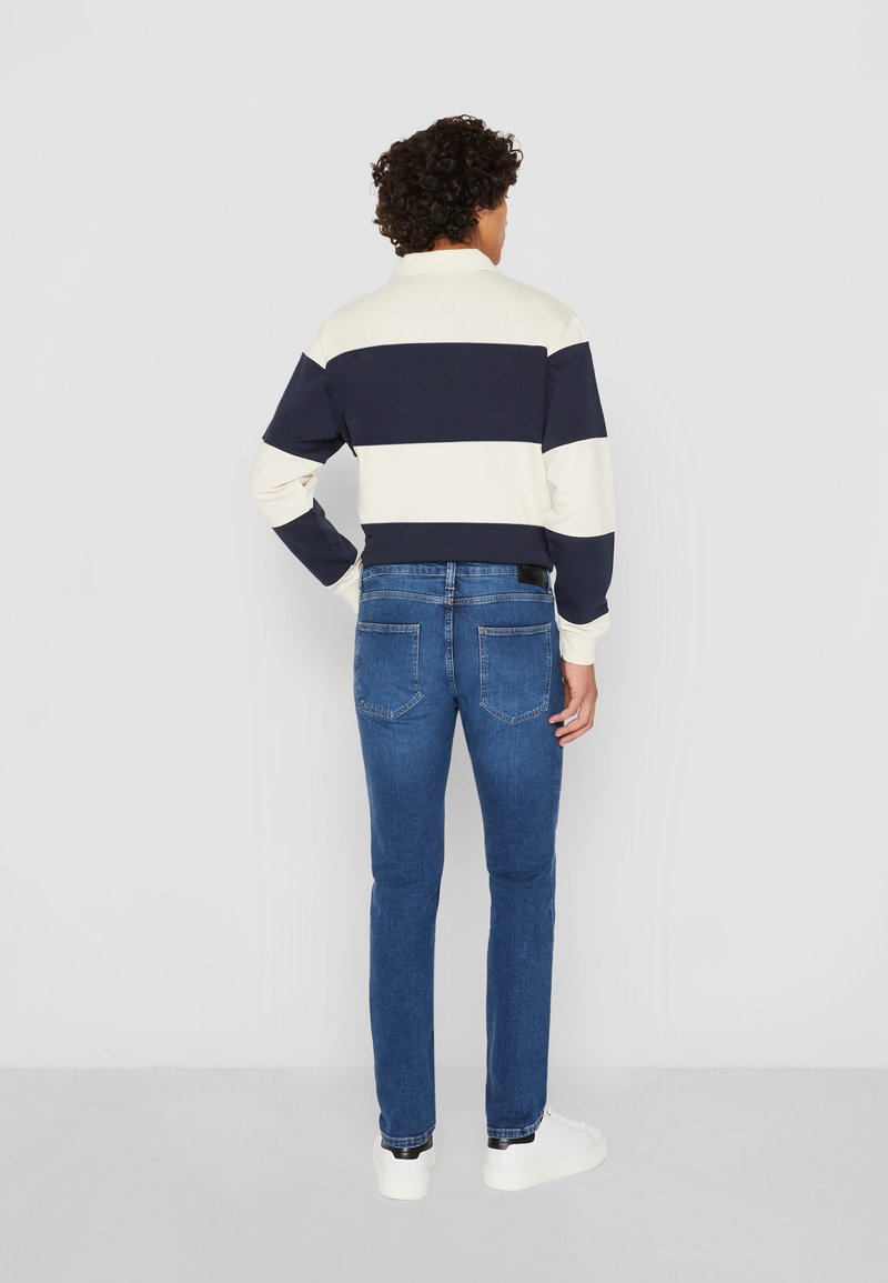 Pull rayé crème et marine, avec un col. Associé à un jean bleu ajusté. Modèle portant des baskets blanches.