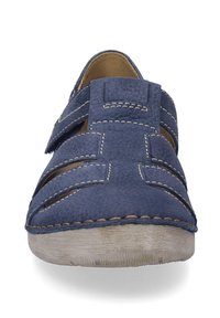 Niebieskie skórzane sandały o fakturowanej powierzchni, z wyciętym wzorem i beżowym przeszyciem. Posiadają płaską podeszwę i otwarte boki zapewniające wentylację.