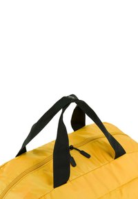 Bolsa de deporte amarilla con asas de cintas negras, cierre con cremallera, textura acolchada y acabado mate. No hay detalles adicionales visibles.