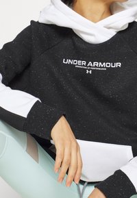 Sudadera en blanco y negro con un patrón moteado, que presenta un bolsillo frontal y un logo. La tela texturizada contrasta con los suaves detalles en blanco.