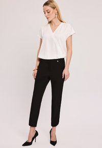 Biała bluzka z krótkim rękawem w stylu kopertowym połączona z dopasowanymi czarnymi spodniami i czarnymi szpilkami; gładki materiał, prosty krój, minimalne wykończenie.