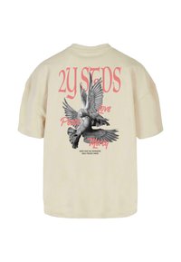 Camiseta de gran tamaño color crema, que presenta una ilustración en blanco y negro de dos palomas y texto en rosa que dice "2Y SEEDS", "Paz", "Amor" y "Misericordia."