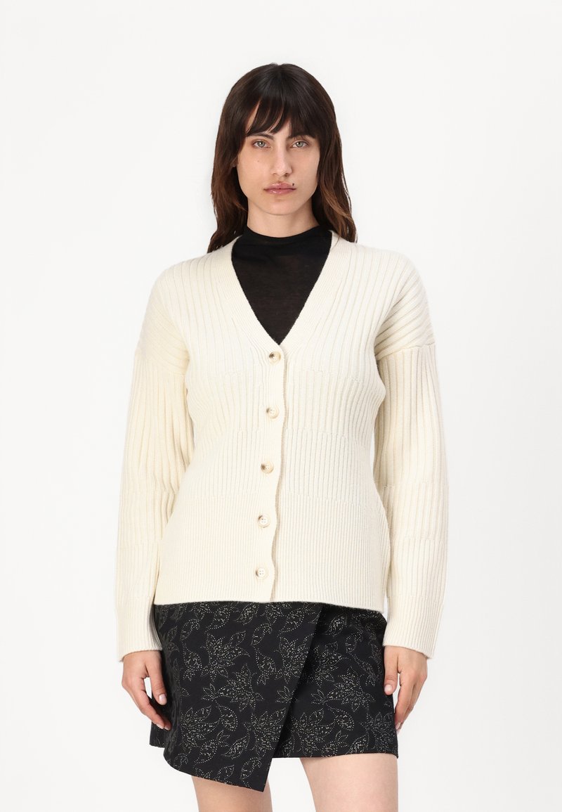 Cardigan a coste color crema con maniche lunghe, caratterizzato da un collo a V, sei bottoni beige sul davanti, abbinato a una gonna nera a fantasia.