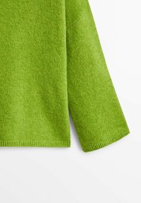 Manche et bas d'un pull en laine vert vif avec une texture douce visible sur fond blanc.