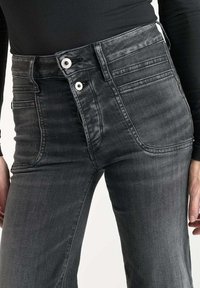 Jeans de mezclilla grises de tiro alto que cuentan con dos botones frontales, bolsillos laterales y un acabado ligeramente texturizado con una silueta ajustada.