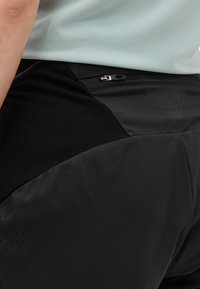 Κοντινό πλάνο ατόμου που φοράει μαύρα αθλητικά σορτς με τσέπη με φερμουάρ και ανοιχτό γκρι υφασμάτινη μπλούζα.