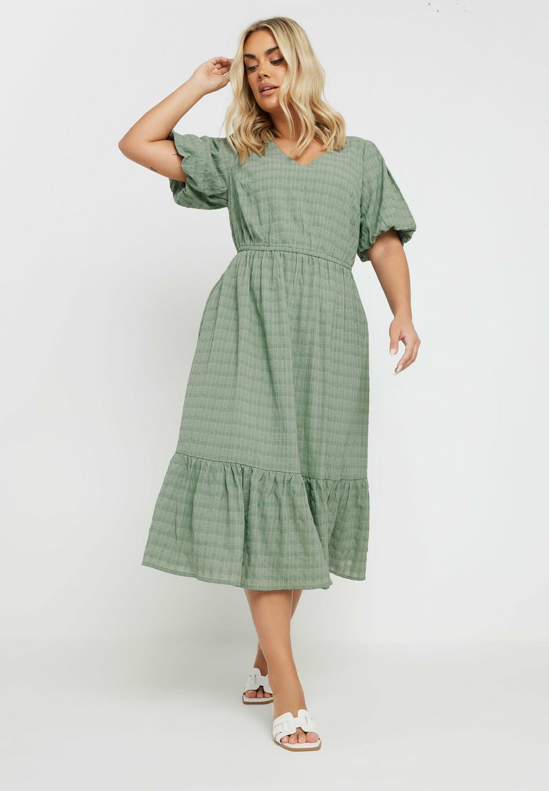 Vihreä ruudullinen midi-mekko, jossa on puffihihat, V-pääntie, joustava vyötärö ja röyhelöhelma. Yhdistetty valkoisiin sandaaleihin.