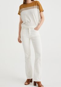 Short-sleeve knit top with brown and beige horizontal stripes, paired with white flared jeans and brown heeled sandals.