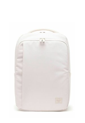 Sac à dos rectangulaire rose clair minimaliste avec poche zippée à l'avant, poignée supérieure et petite étiquette de marque dans le coin inférieur droit.