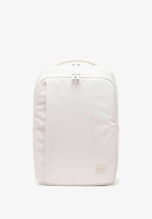 Sac à dos rectangulaire rose clair minimaliste avec poche zippée à l'avant, poignée supérieure et petite étiquette de marque dans le coin inférieur droit.