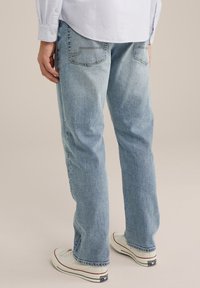 Svetlo modri denim hlače z ravnim krojem, z zadnjimi žepi in rahlim bledenjem, v kombinaciji z belimi platnenimi supergami.