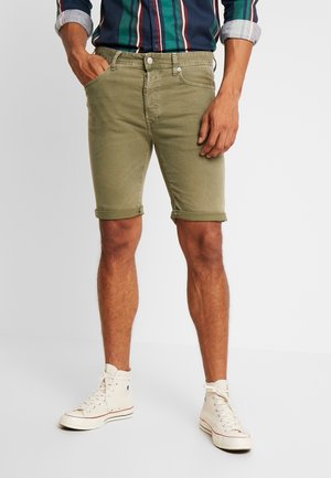 Olijfgroene denim shorts met opgerolde zomen, voorzien van zakken aan de voorkant en een ritssluiting, gecombineerd met witte hoge sneakers.