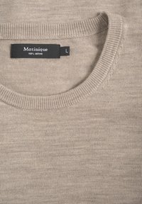 Pulover din lână merino de culoare bej deschis, cu guler rotund, manșete și tiv cu nervuri. Dispune de o etichetă neagră cu inscripția "Matinique" și mărimea "L". Textură moale.