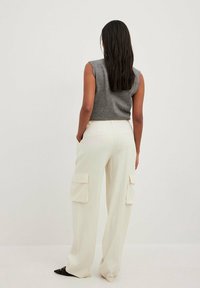 Grijze mouwloze top gecombineerd met crèmekleurige cargobroek met grote zijzakken, een losse pasvorm en een gladde textuur. Achteraanzicht getoond.