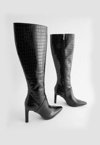 Črne škornje do kolen, narejene iz sijočega materiala s krokoembossnim vzorcem, z ostrimi prsti in 10-centimetrskimi stiletnimi petami ter stransko zadrgo.