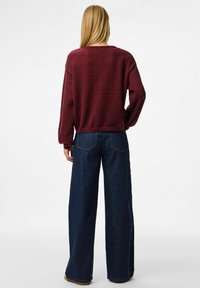 Burgundin neulottu neule, jossa on väljä malli ja ribbireunat, yhdistettynä leveälahkeisiin tummiin farkkuihin, joissa on korkea vyötärö ja takataskut.