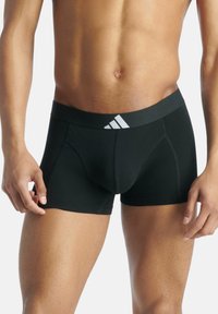 Boxers en coton noir avec une large ceinture élastique arborant un logo blanc. Texture lisse, design ajusté et longueur mi-cuisse.